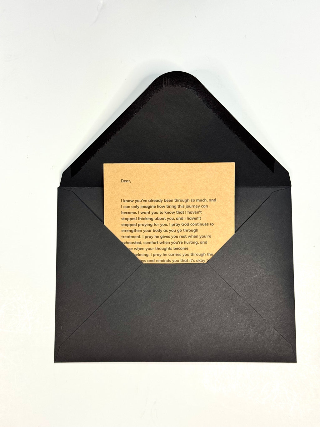 A black envelope with a triangular flap opening, containing a tan kraft paper card with printed text, photographed on a plain white background.