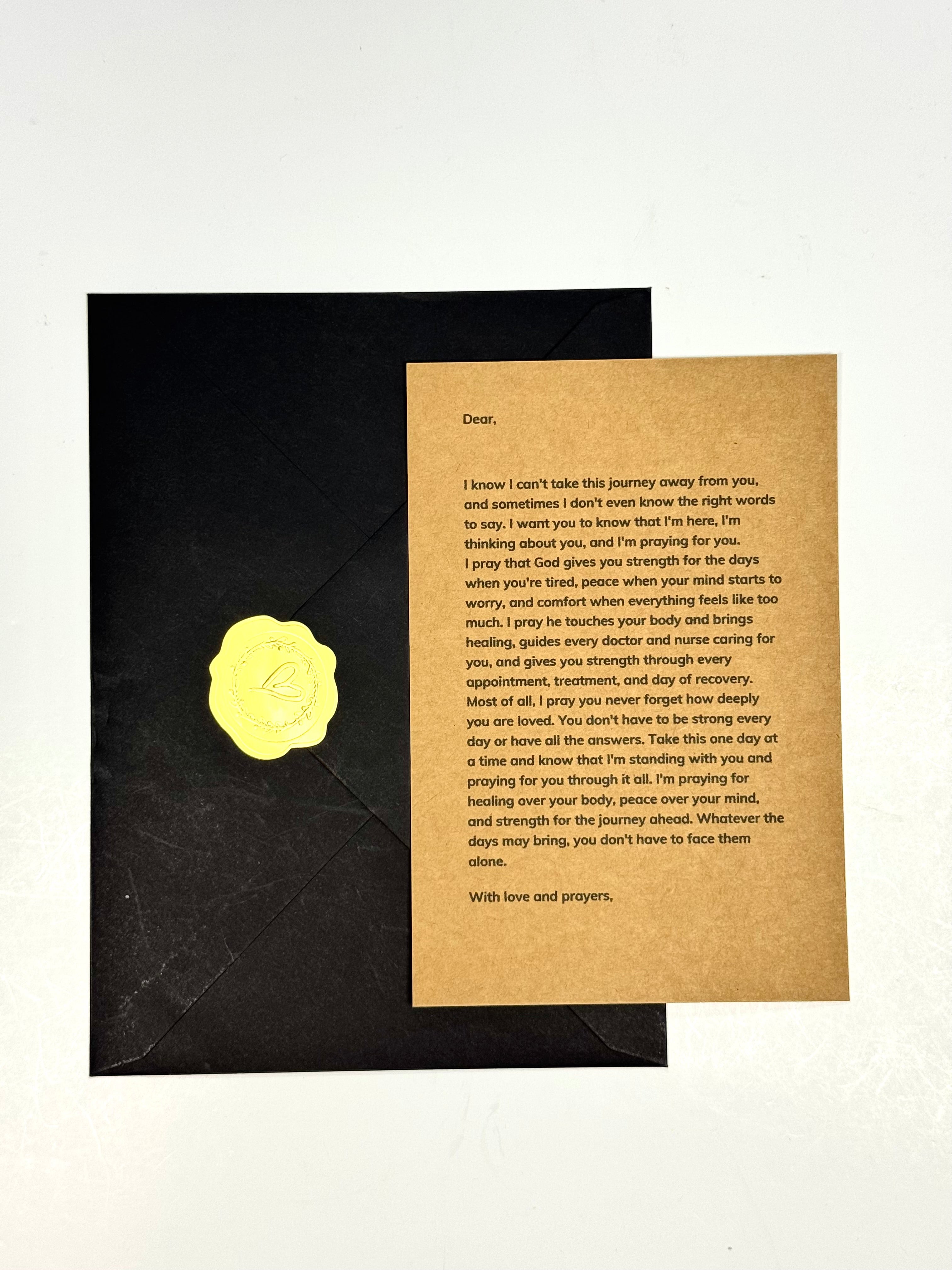 A square printed card with a handwritten letter on a tan paper background, placed on top of a black square card with a yellow circular sticker, photographed against a white background.