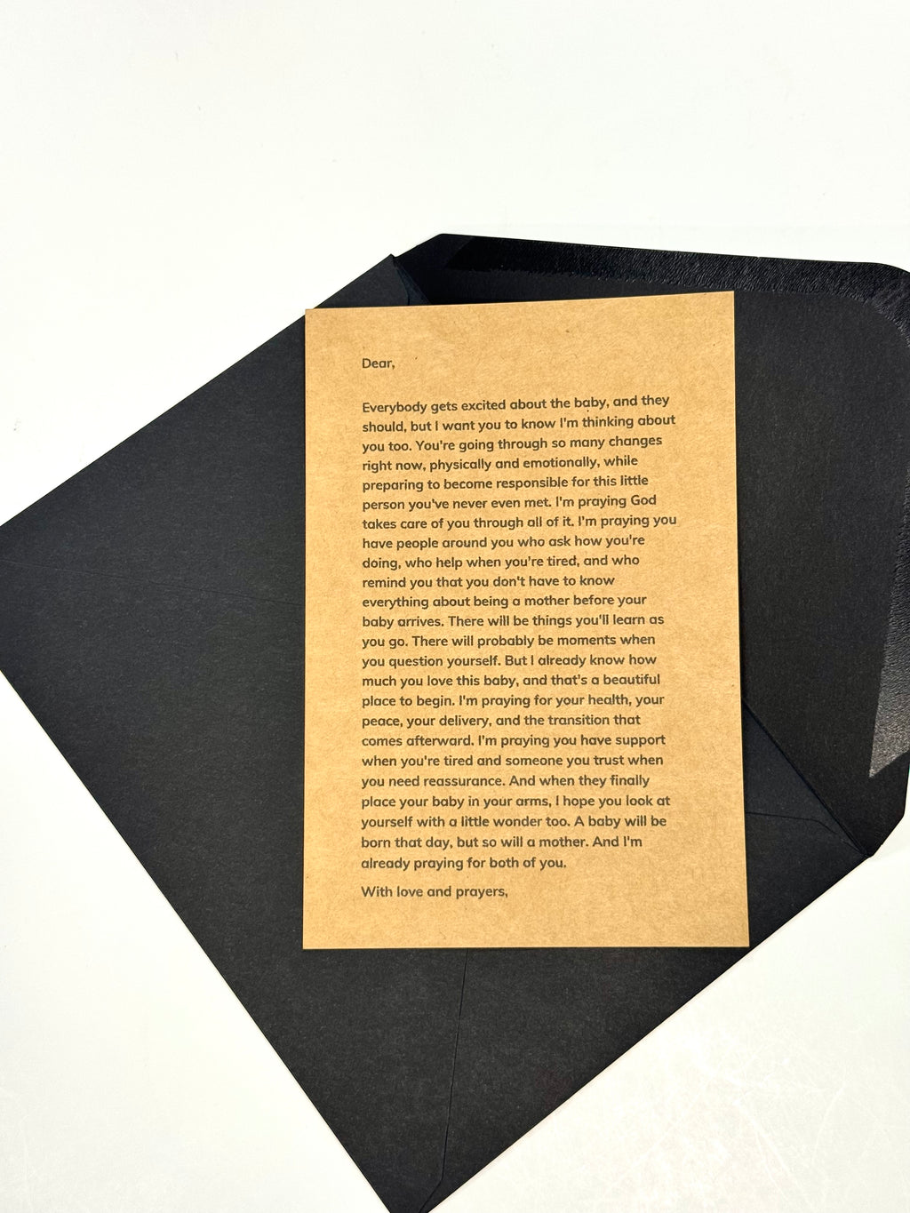 A black envelope or book-like package laid on a white background, with a tan prayer card addressed inside, photographed from above at an angle.