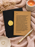 A styled flat-lay of a handwritten apology letter on a brown kraft paper card, sealed with a gold wax stamp, placed on a black envelope over a pink knit blanket. A white candle, dried flowers, a wooden spoon with a heart, and a gold pen are arranged around it.