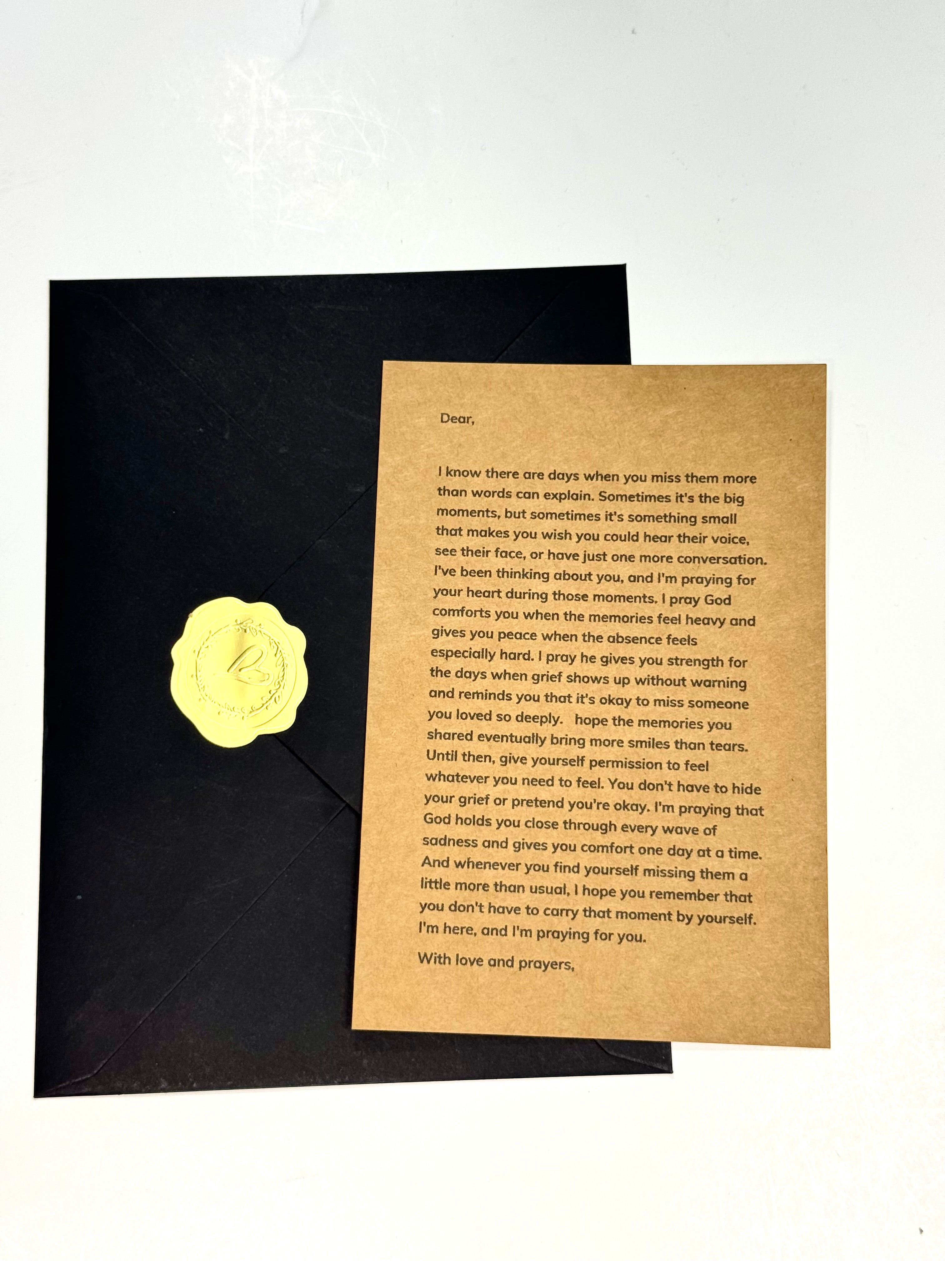 A square black plaque or mat with a centered beige prayer card, photographed against a white background.