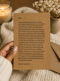 A handwritten condolence card on brown kraft paper with printed text, placed on a white textured blanket with a warm candle in the background.