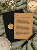 A brown kraft paper prayer letter with a gold wax seal, styled in a cozy flat-lay with a black envelope, white baby's breath flowers, a lit candle, a gold pen, and a green knit blanket.