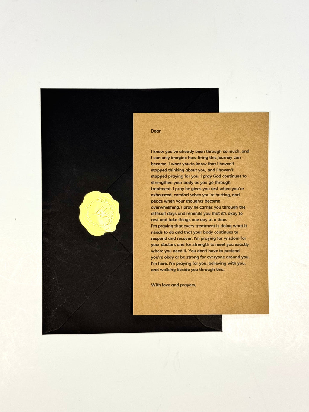 A black envelope with a gold foil seal lies on a white background next to a handwritten condolence card on a textured beige cardstock.