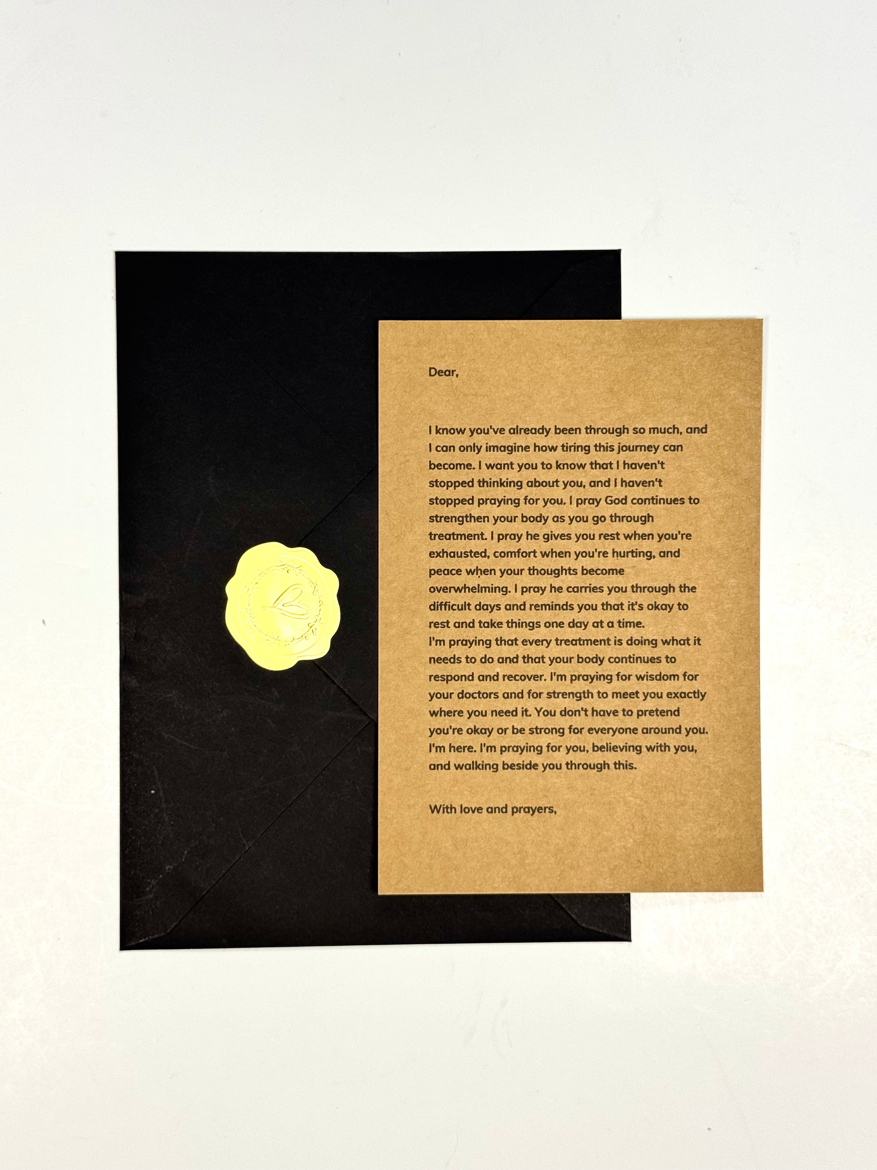 A black envelope with a gold foil seal lies on a white background next to a handwritten condolence card on a textured beige cardstock.