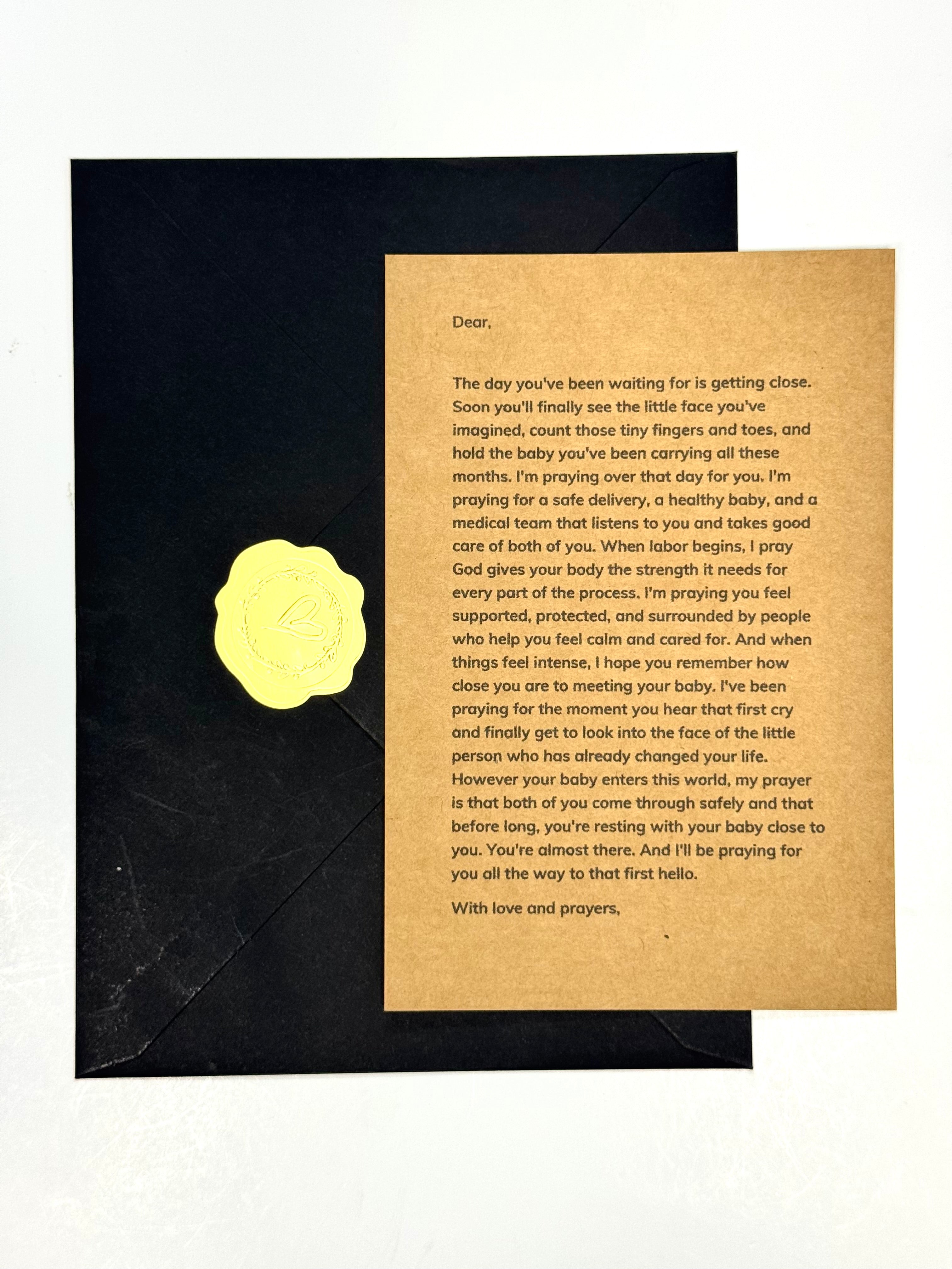 A baby shower card featuring a black envelope with a gold foil seal and a tan parchment-style insert with printed baby development text, shown on a white background.