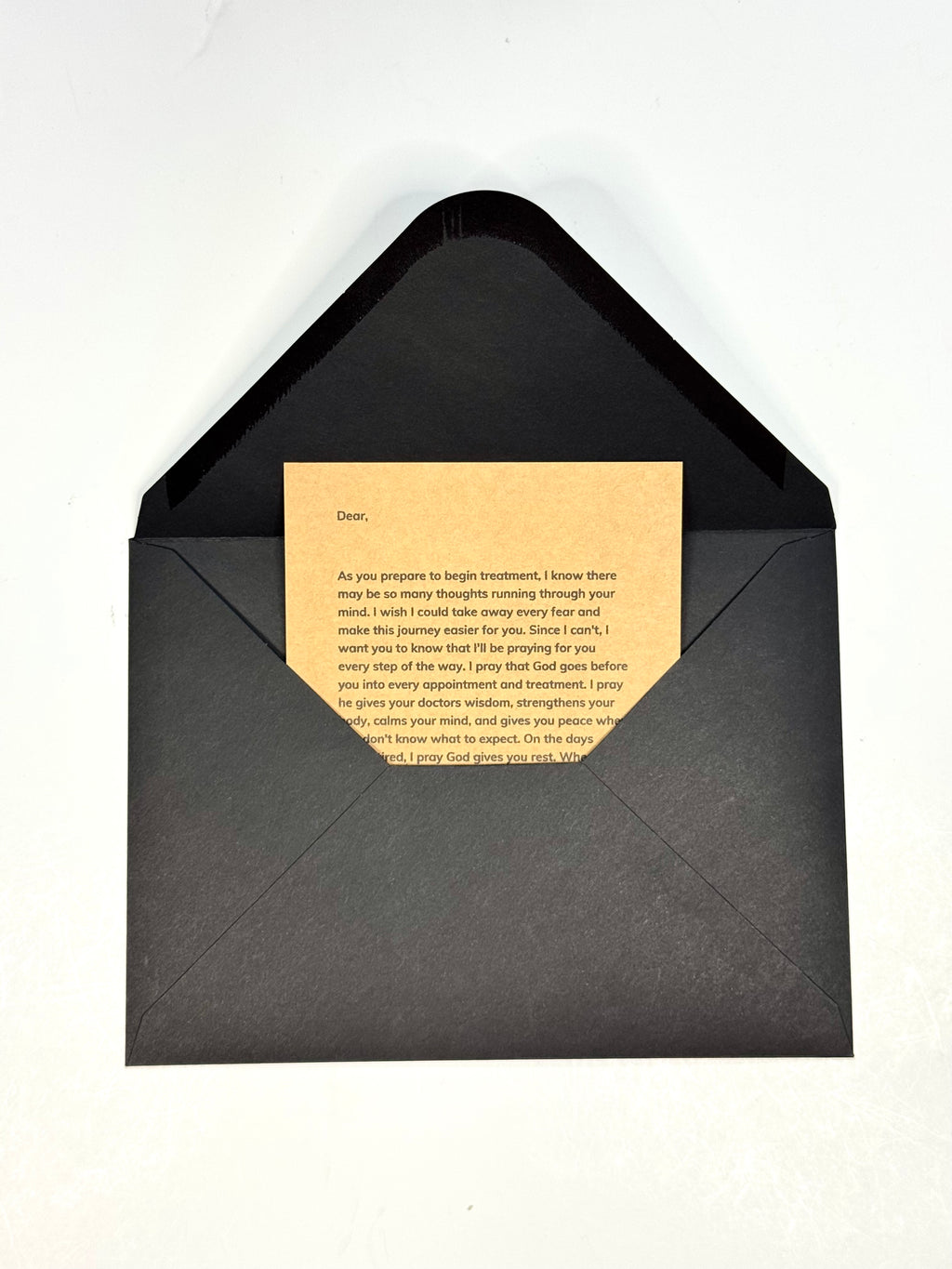 A black envelope with a textured finish, opened to reveal a beige card with printed text inside, set against a plain white background.