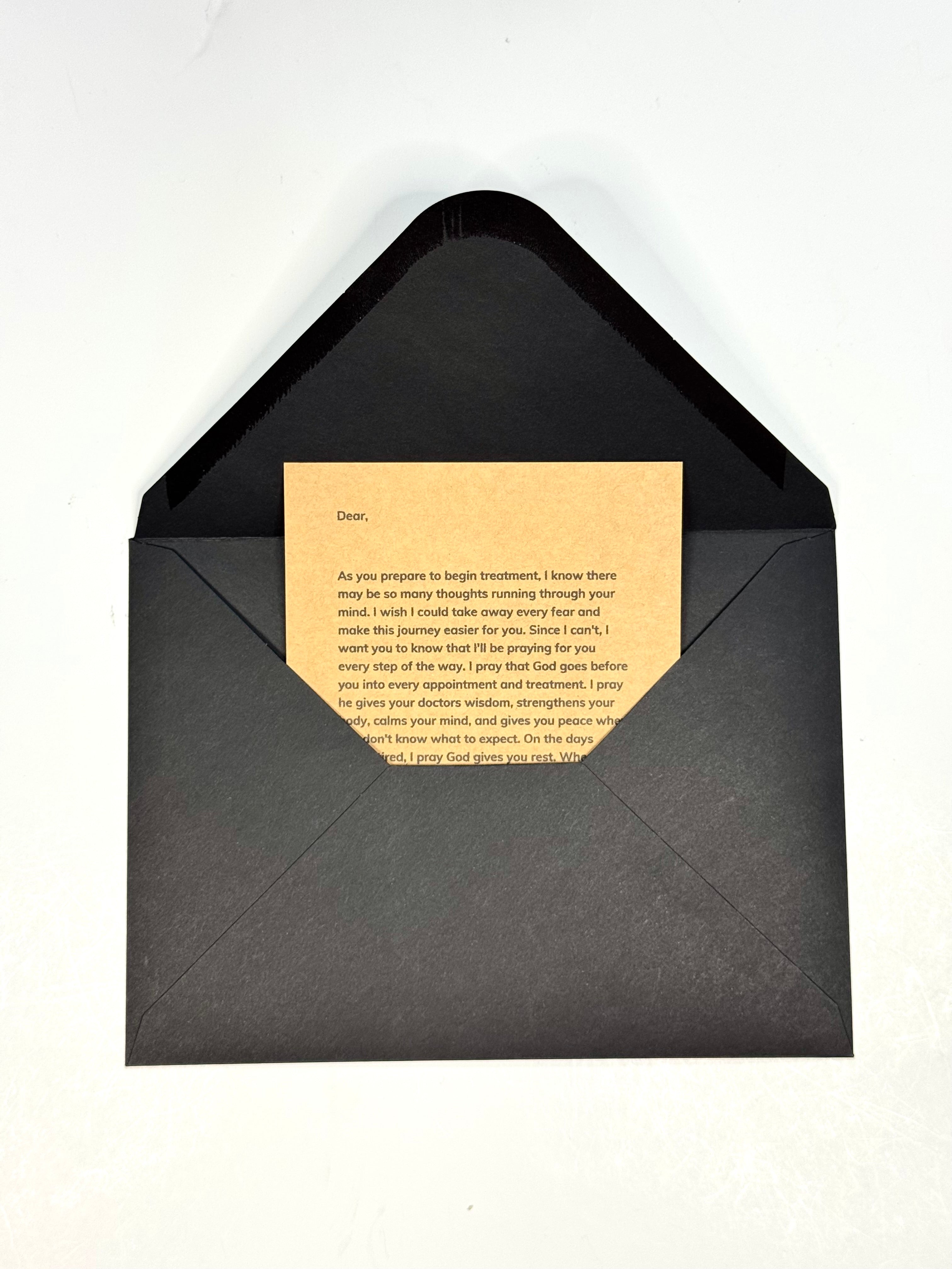 A black envelope with a textured finish, opened to reveal a beige card with printed text inside, set against a plain white background.