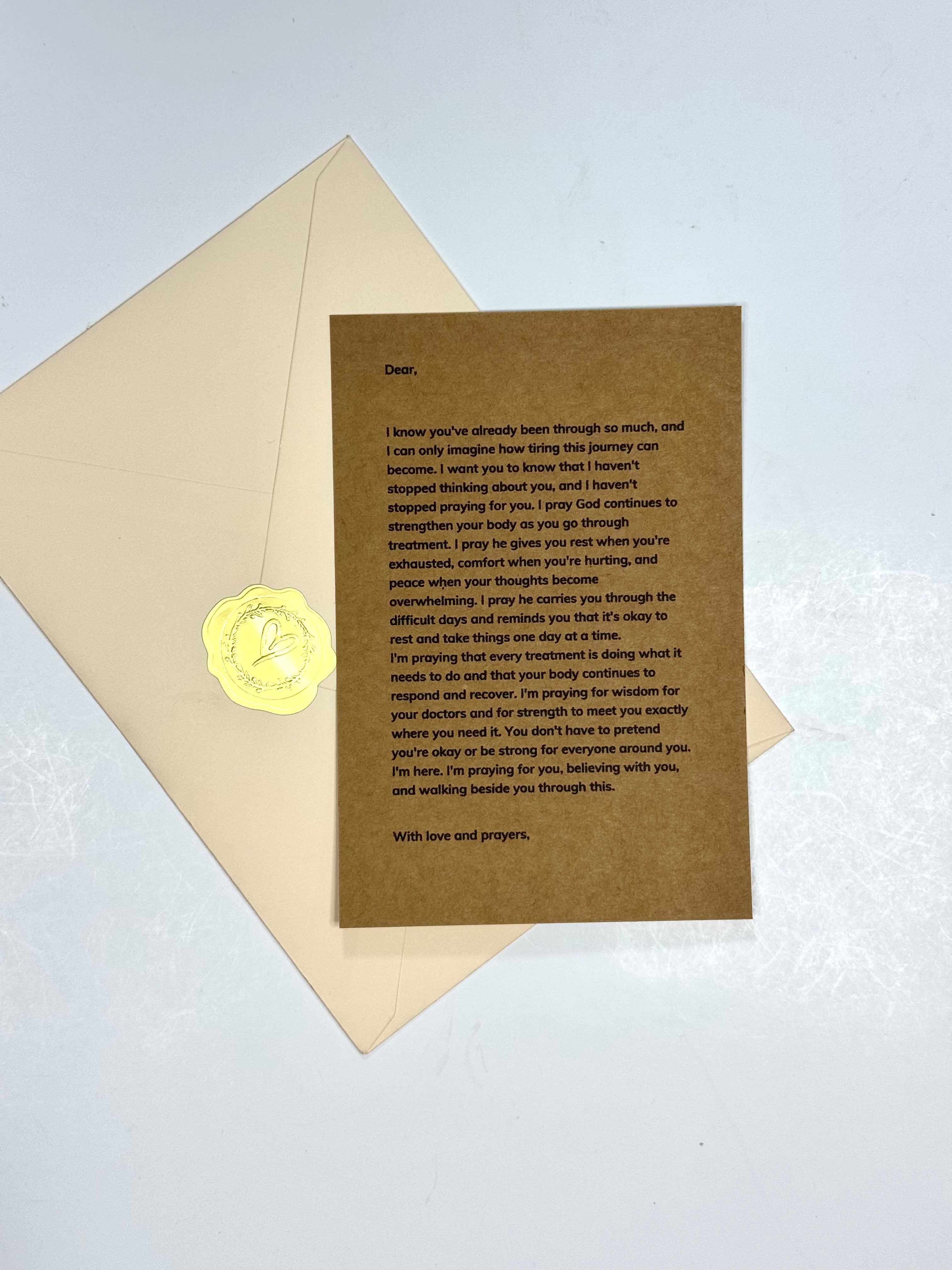 A brown kraft paper prayer card with printed black text, placed on top of a cream envelope with a gold wax seal, on a light blue background.