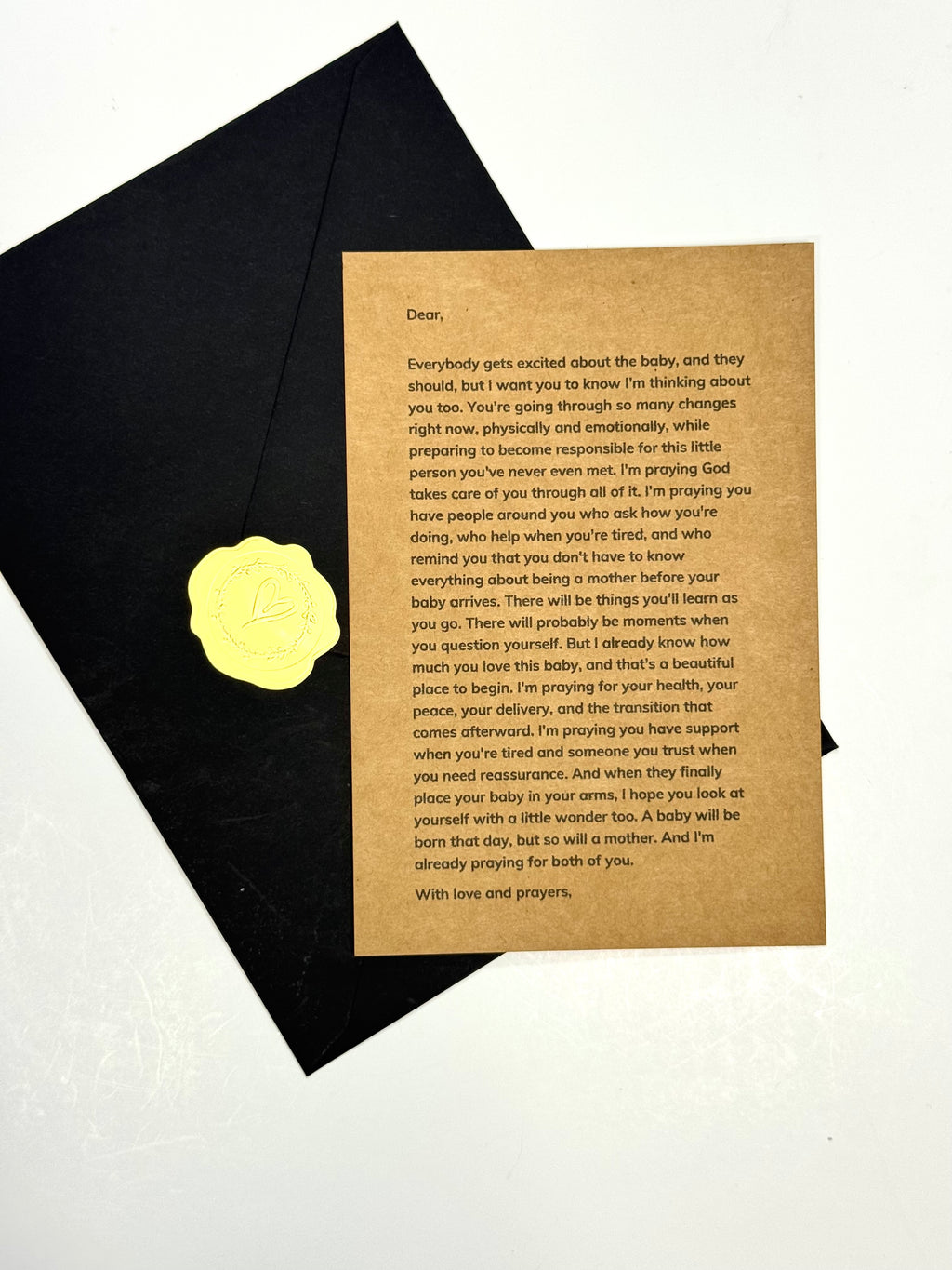 A printed sympathy card with a warm tan background and black text, placed on top of a folded black envelope against a white background.