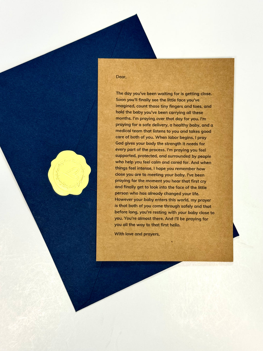 A square kraft paper condolence card with printed sympathy text, placed on top of a dark blue envelope against a white background.