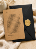 A kraft paper condolence card with printed sympathy message, sealed with a round gold wax seal, attached to a black envelope on a soft beige fabric background.