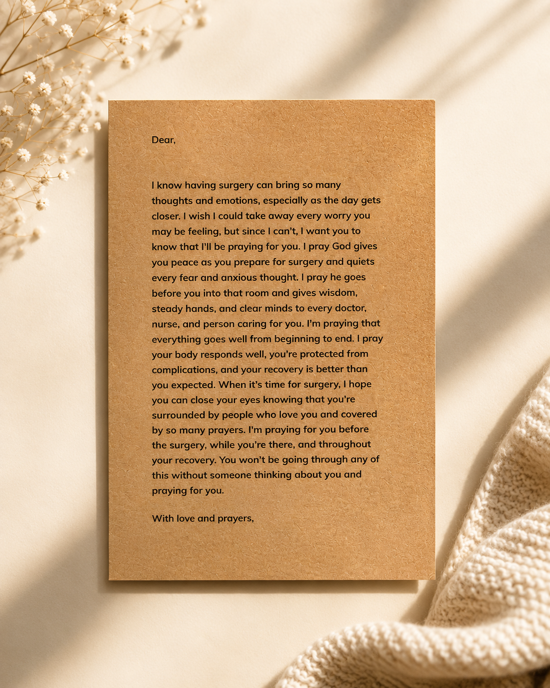 A printed sympathy card with a warm brown kraft-paper look, laid flat on a light beige fabric background with soft shadows and dried flowers in the corners.