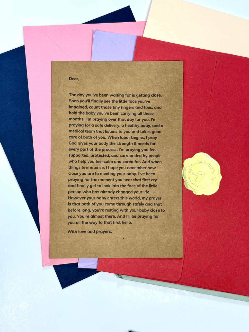 A printed sympathy or remembrance card with a brown kraft-paper style body and a gold embossed seal, shown layered over red, pink, and navy envelopes on a light background.