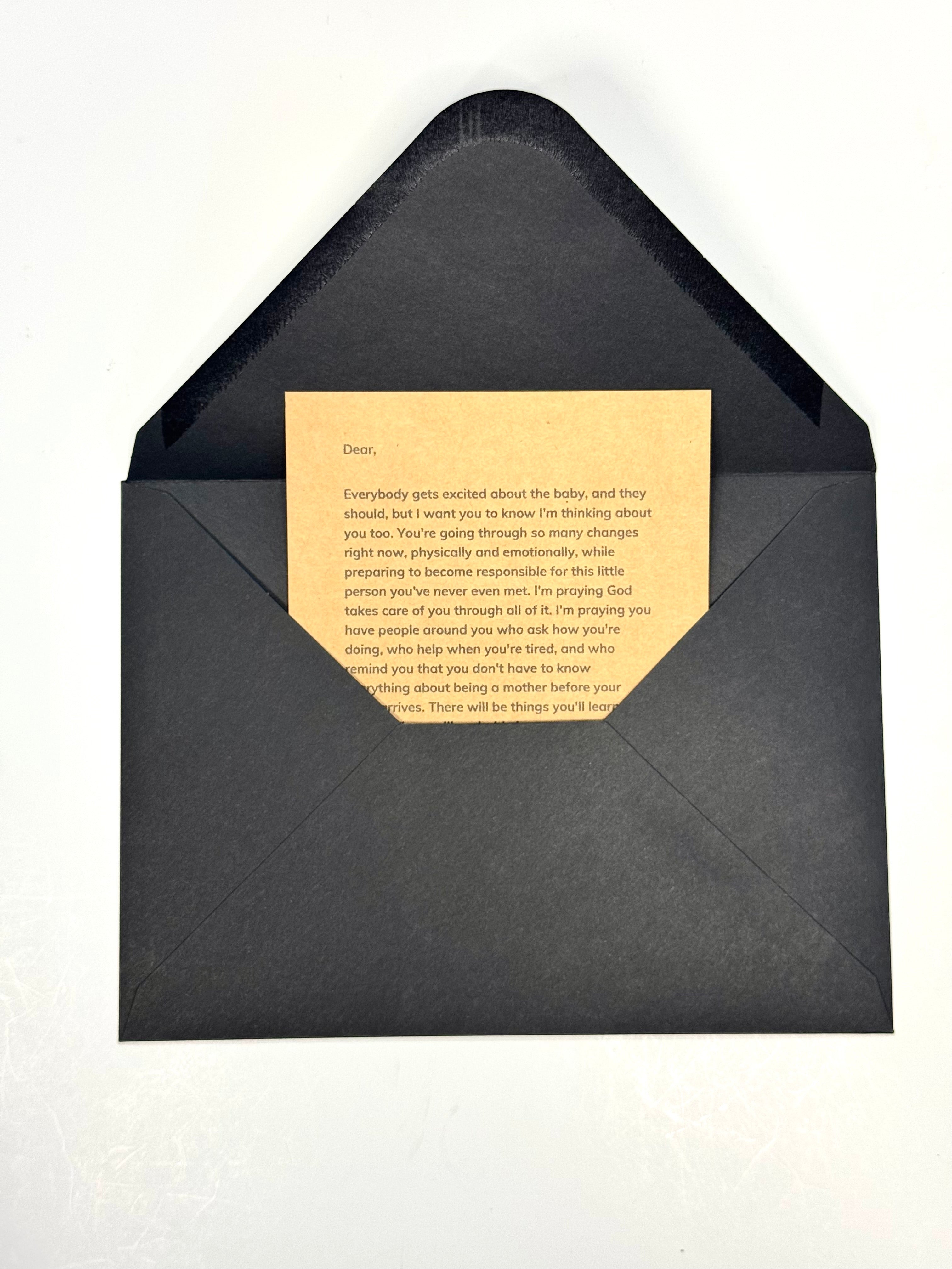 A black envelope with a rectangular flap open to reveal a centered beige card with printed text, photographed on a plain white background.
